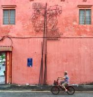 Woman riding a bicycle next to a pink building
